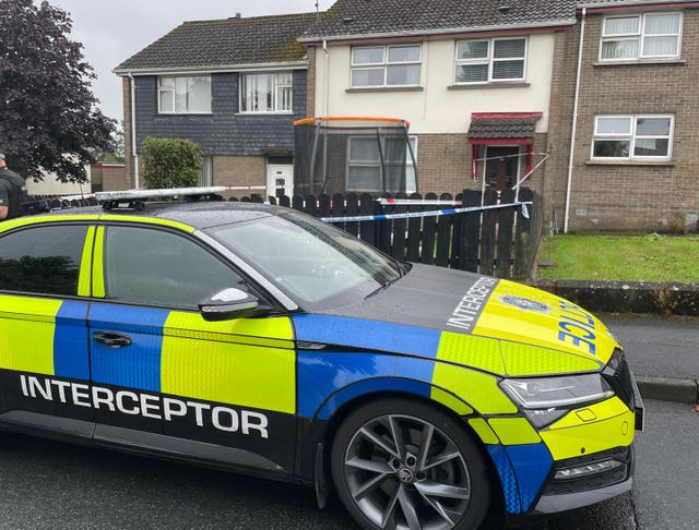 A police vehicle outside a terraced house, which is surrounded by police tape