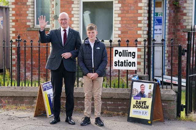 John Swinney waves standing alongside his son Matthew outside a polling station