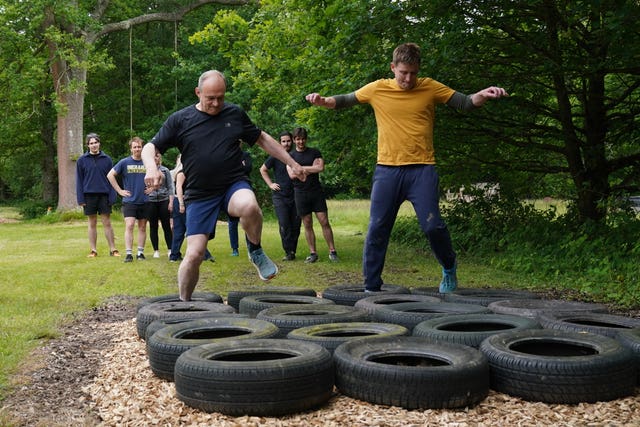 Sir Ed Davey in a black t-shirt and shorts and Mike Martin in an orange top and tracksuit bottoms try to step in the middle of some tyres on an assault course