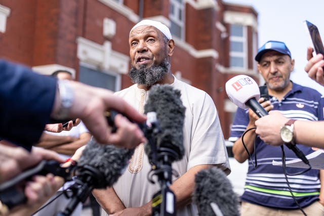 A mosque chairman stands surrounded by media with microphones and camera 