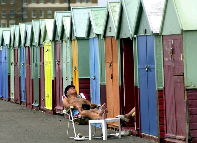 A bather optimistically hopes for sunshine in front of empty Brighton beach huts