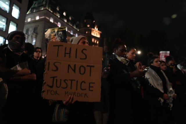 A crowd of people hold cardboard signs, one reads 'this is not justice for murder'