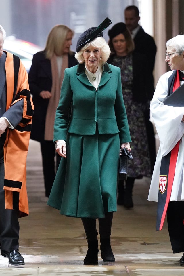 Camilla wearing a dark green blazer and skirt with a feathered hat
