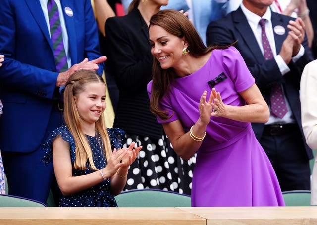 Kate leans towards Charlotte as they both stand and clap in the royal box at Wimbledon's Centre Court